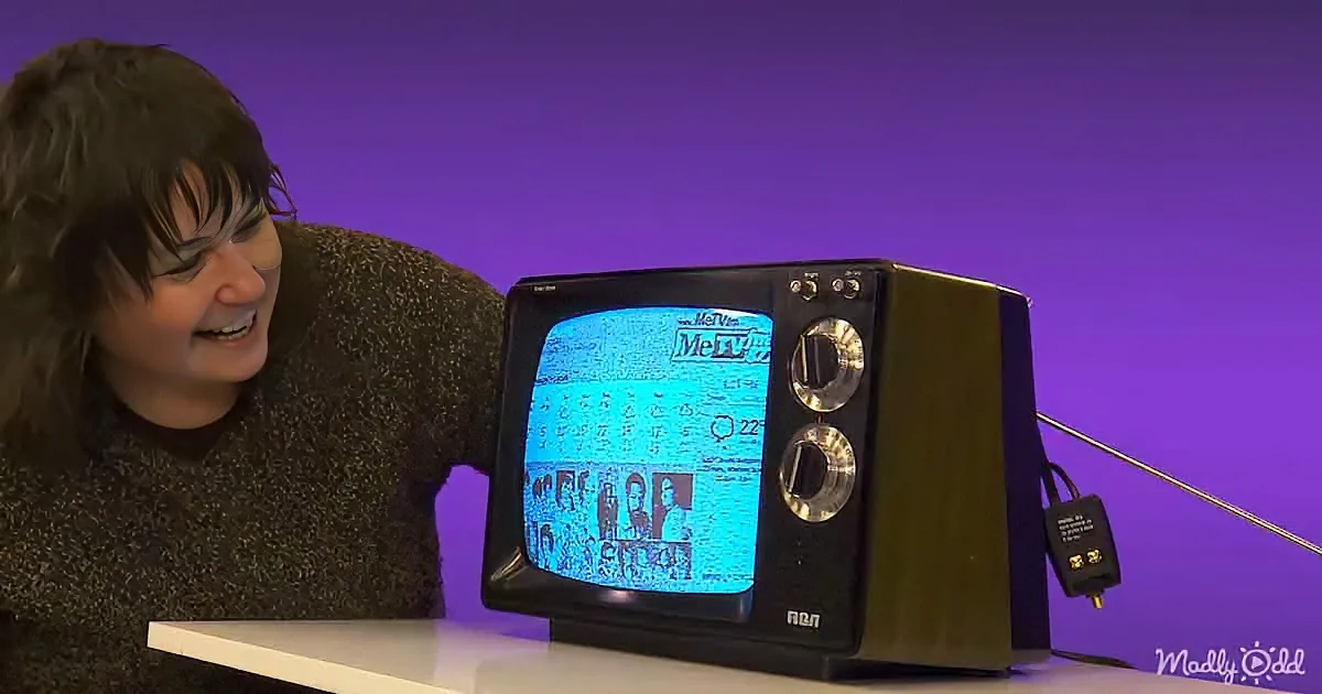 A person leans over a small black CRT TV with a MeTV logo, displaying static and a few images.