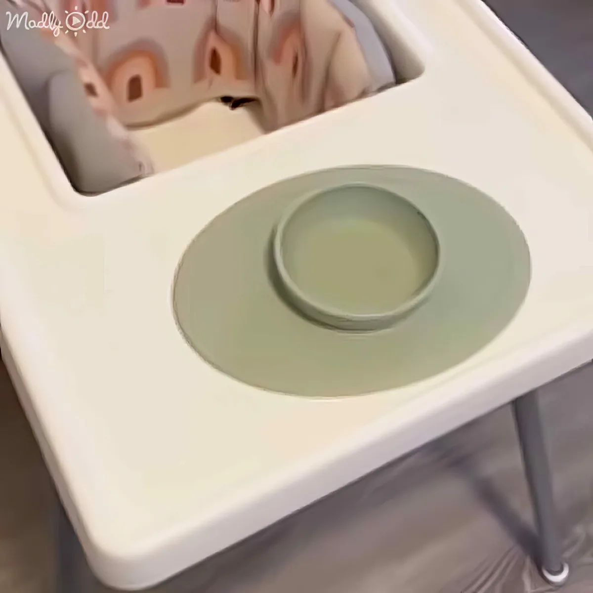 A high chair with a green tray and a baby's face partially visible in the background.