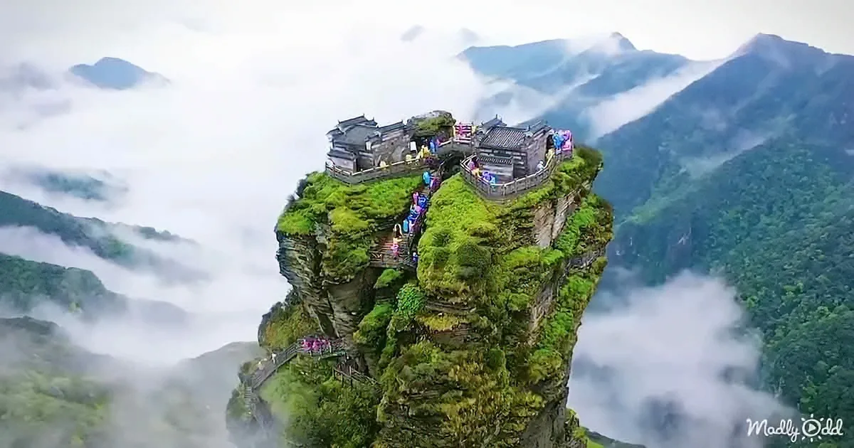 A lush, moss-covered cliff with a traditional building perched on its edge, surrounded by misty mountains.
