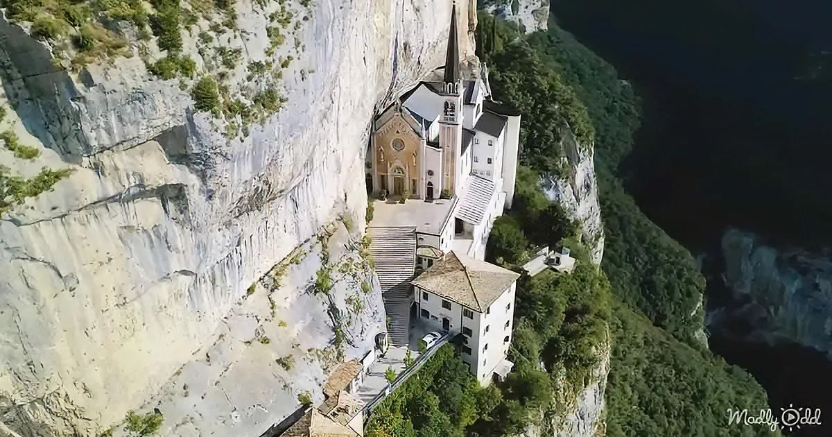 A stunning church built into a cliff face, surrounded by lush greenery and a dark valley below.