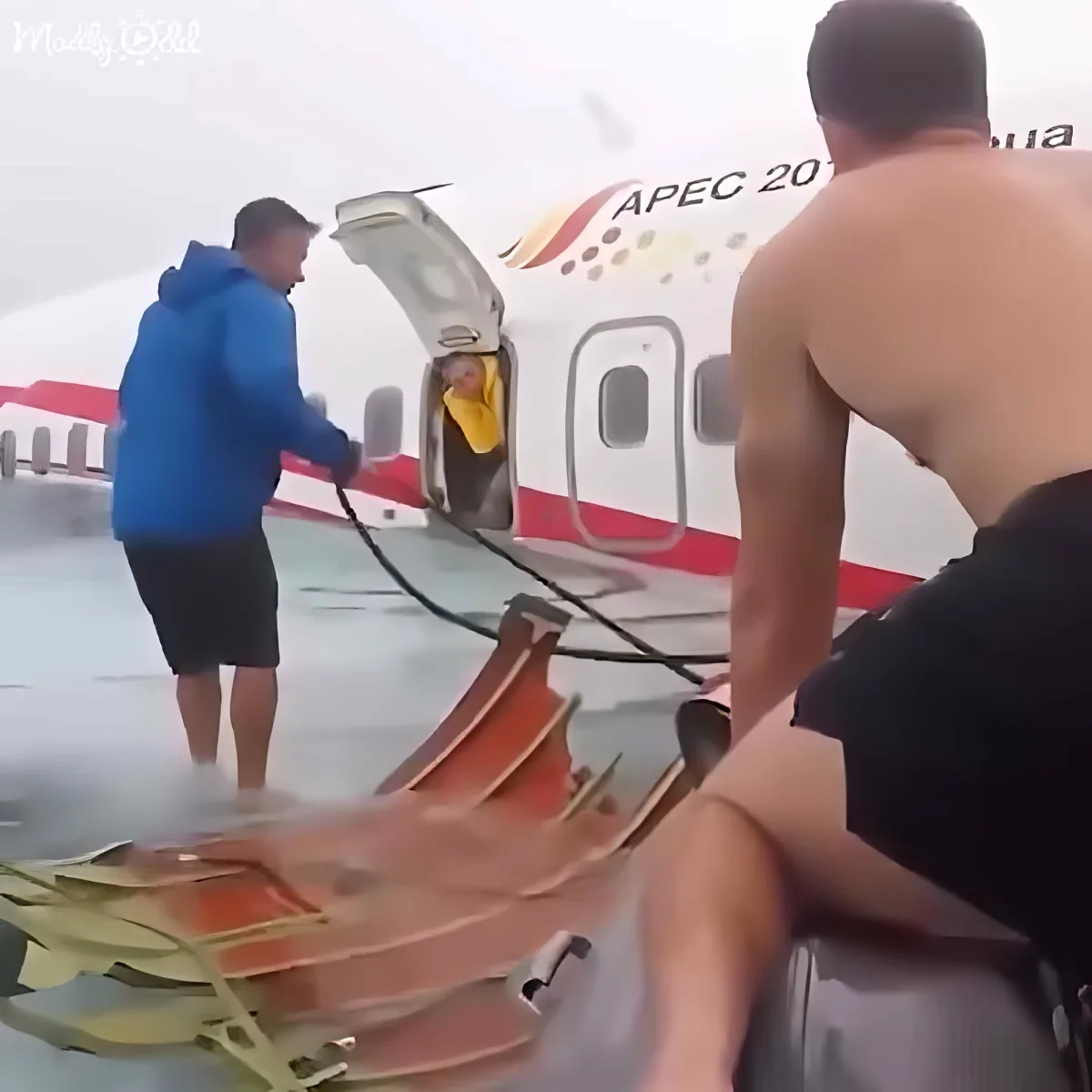 A shirtless man climbs a ramp into an airplane with another person assisting.