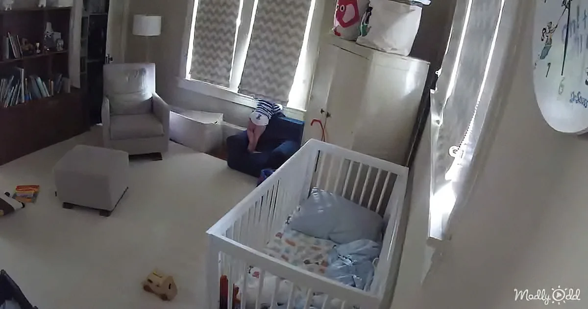 A baby's crib with a blue blanket and toys, near a window with curtains, in a room with a chair and bookshelf.