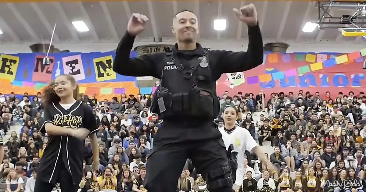 A police officer dances enthusiastically in front of a cheering crowd at a school event.