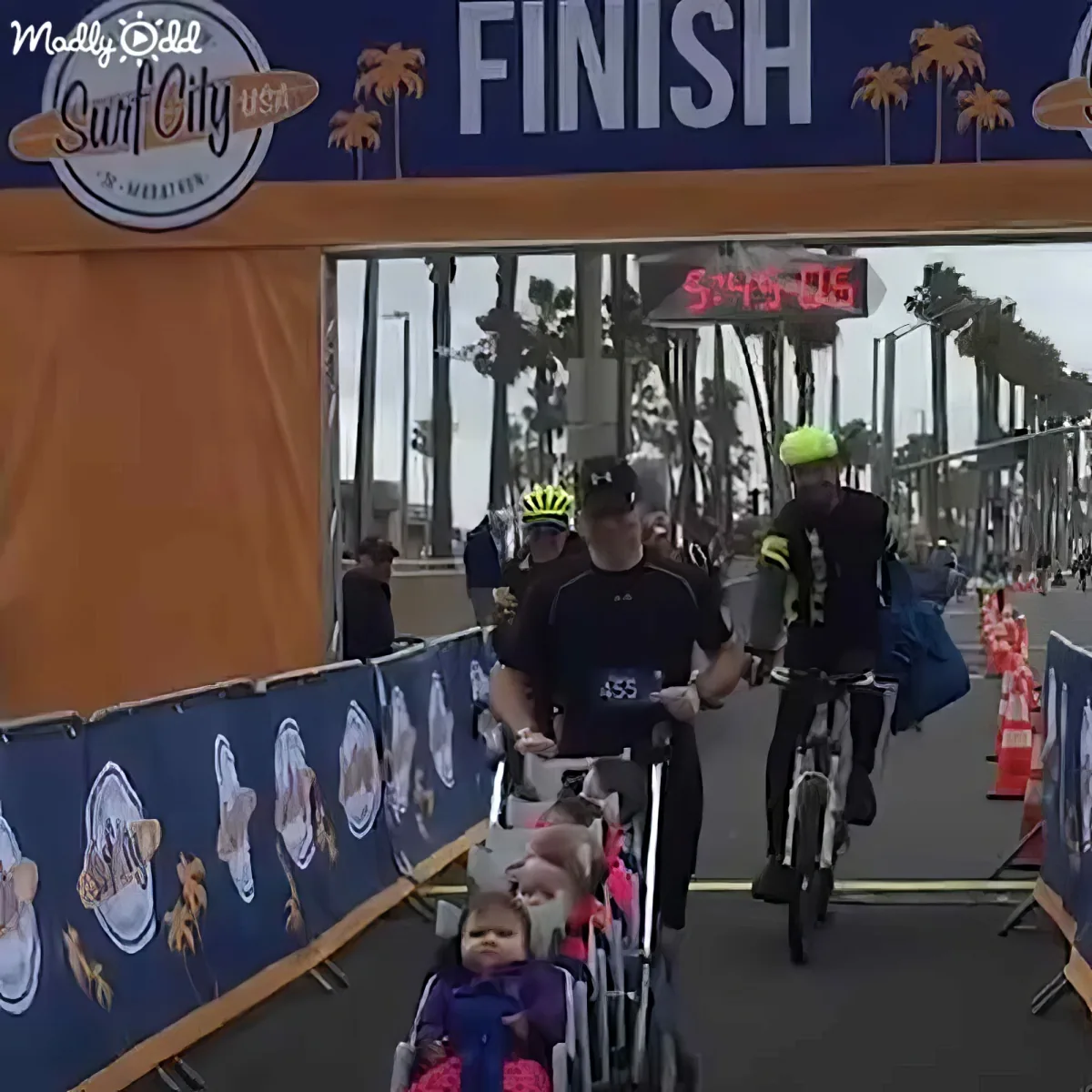 A man rides a bike with a baby carriage at the finish line of a race.