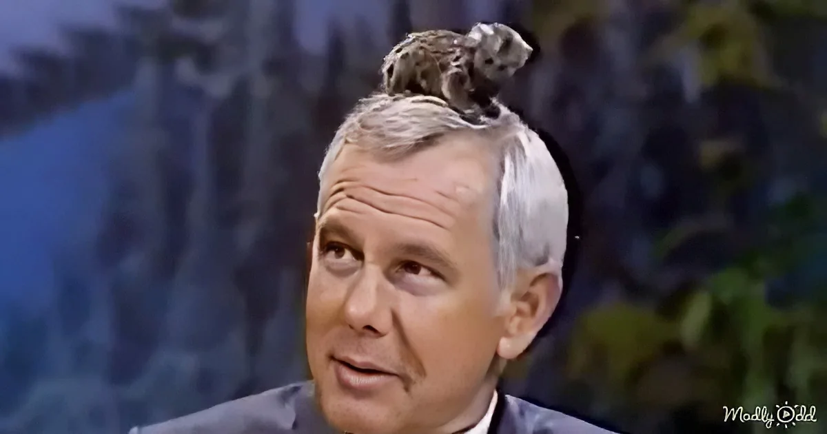 A man with a bird perched on his head, wearing a suit, against a blurred background.