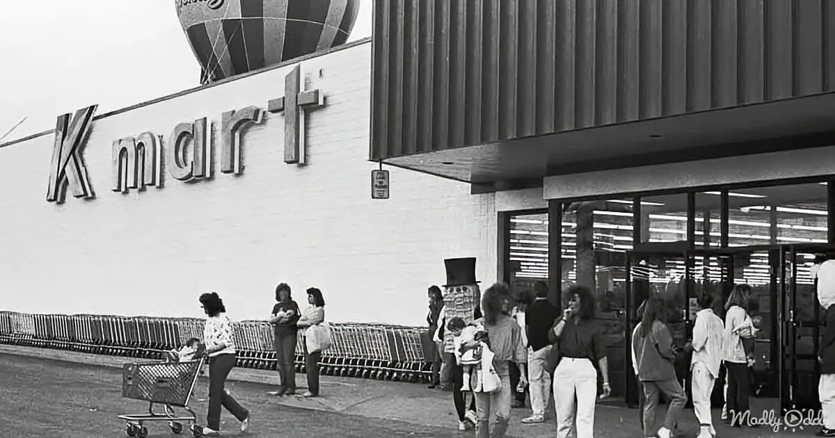 People gather outside a Kmart store with shopping carts and a hot air balloon in the background.