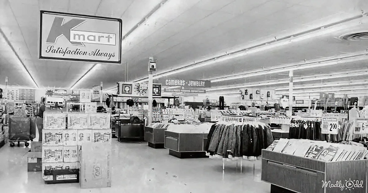 A vintage Kmart store interior with "Satisfaction Always" sign, neatly arranged shelves, and a variety of products.