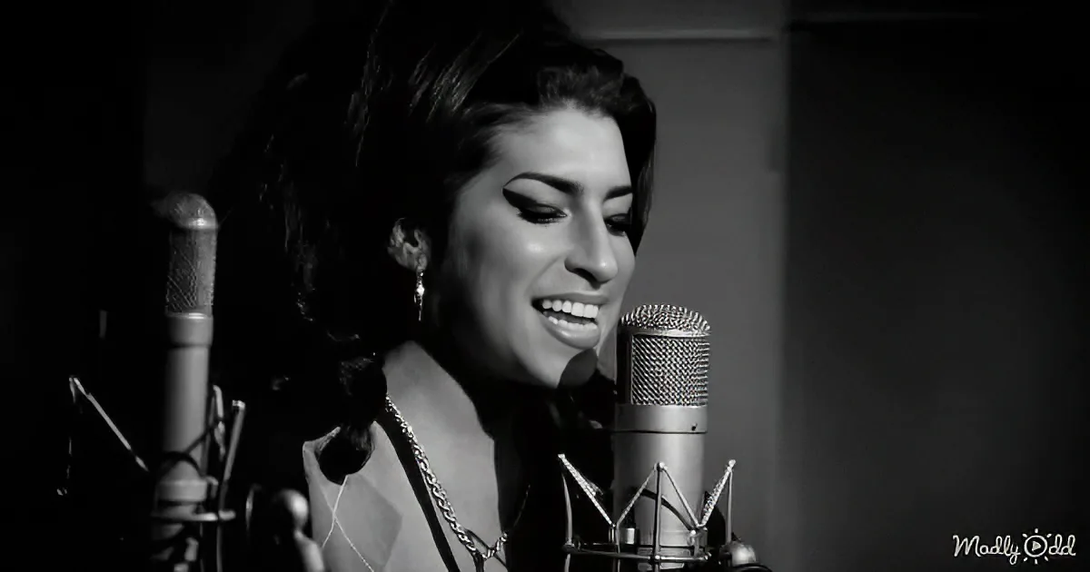 A woman sings into a microphone in a recording studio, wearing a necklace and earrings.