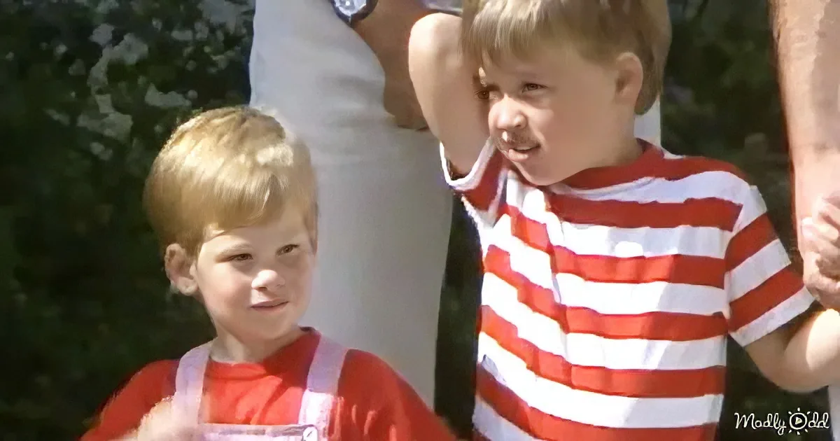 Two young boys in red and white striped shirts stand outdoors, one smiling, the other looking down.
