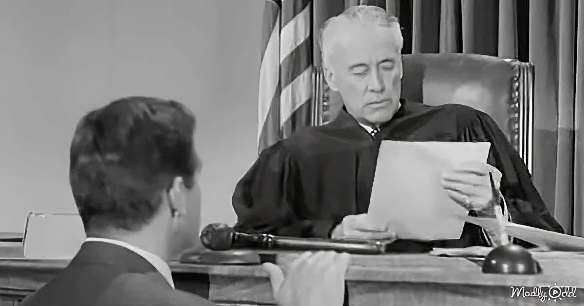 A judge in a courtroom reads a document while a lawyer listens attentively.