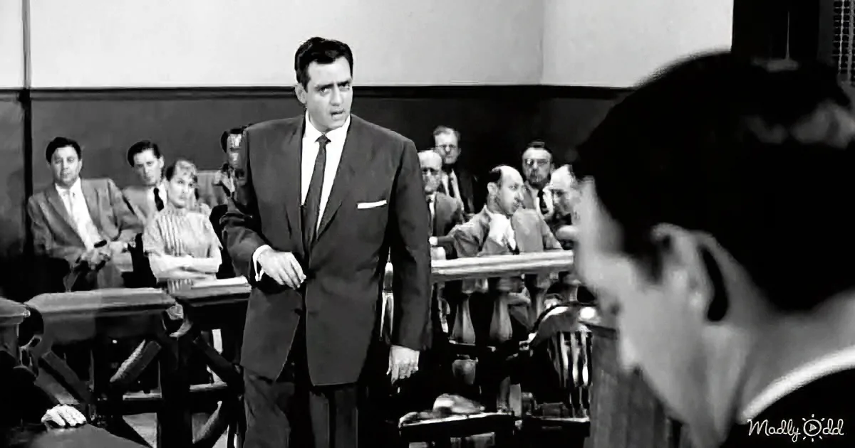 A man in a suit stands in a courtroom, gesturing as he speaks, with a jury and spectators in the background.