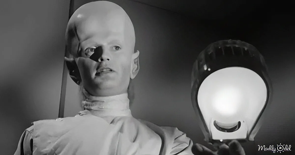 A person with a bald head and a white turtleneck is holding a glowing object.