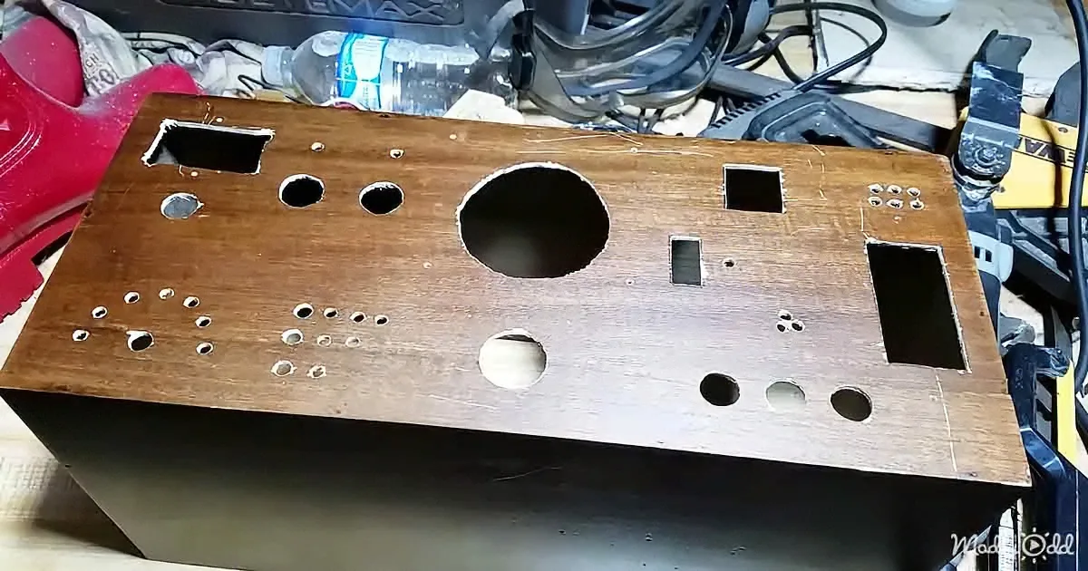 A wooden box with various holes and cutouts sits on a cluttered workspace.