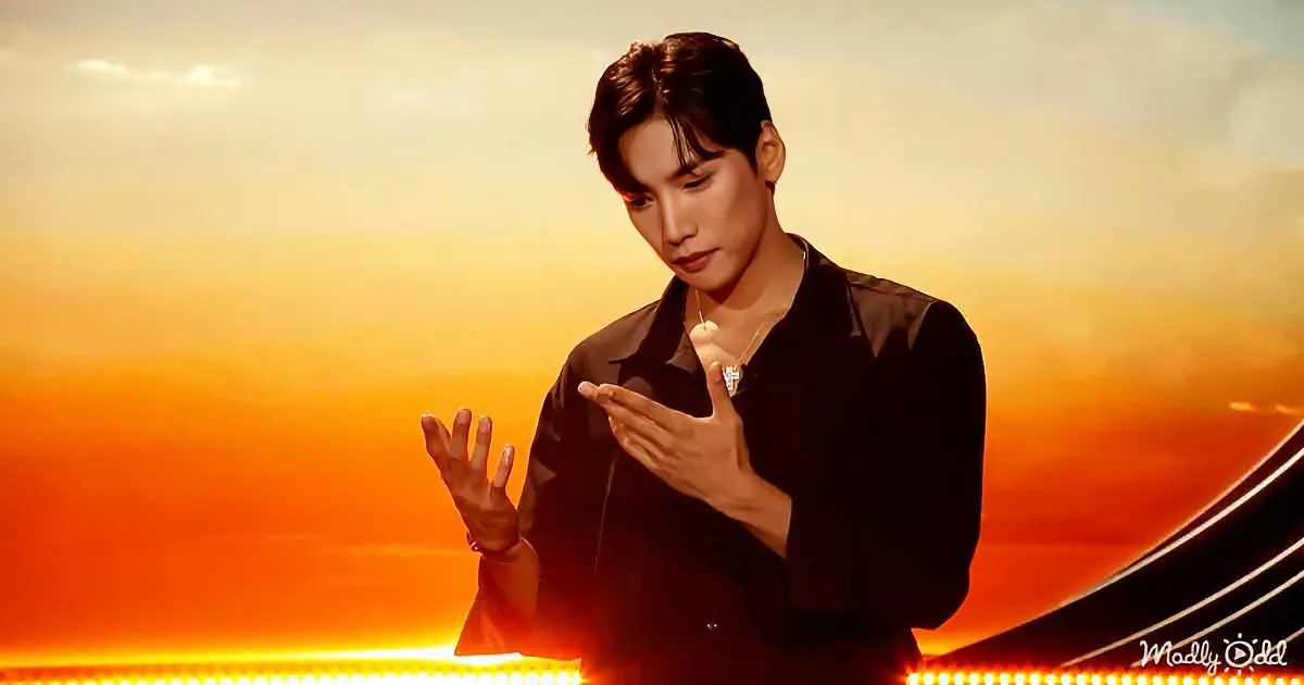 A person in a black shirt stands against a sunset backdrop, gesturing with their hands.