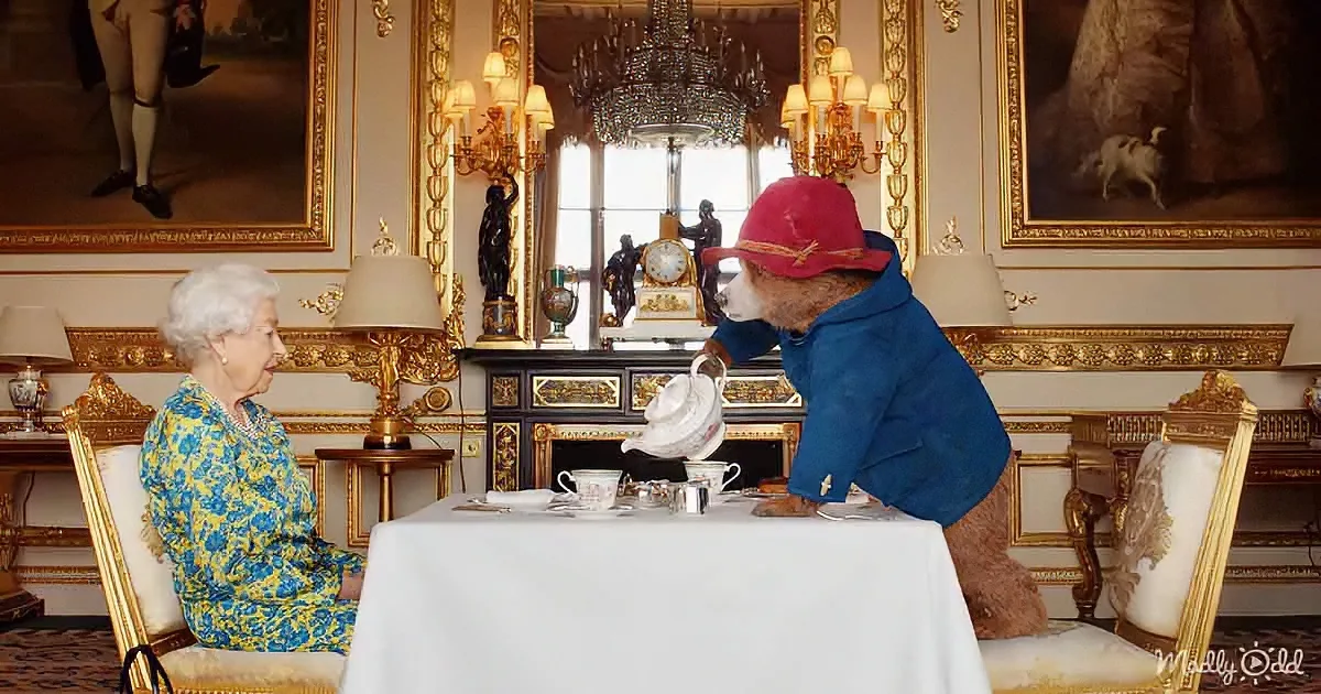 Paddington Bear pours tea for Queen Elizabeth II in a grand, ornate room.