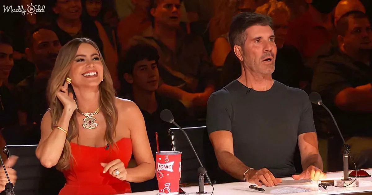 A woman in a red dress laughs while a man in a black shirt looks surprised at a table with microphones and a Sonic drink.