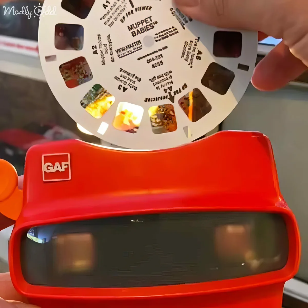 A hand holds a red View-Master with a Muppet Babies reel above it, showcasing a vintage toy.