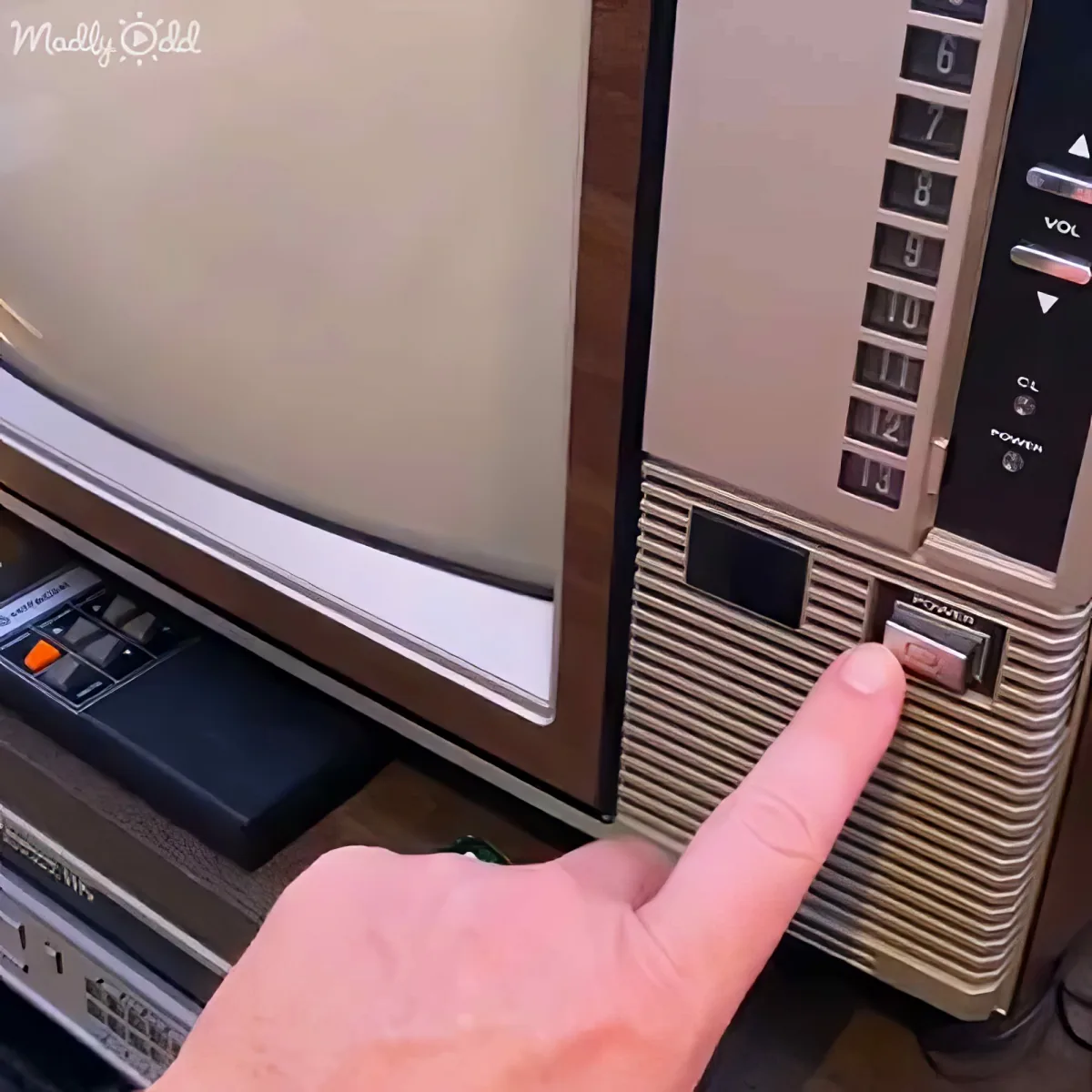 A hand points at the power button on an old, vintage television with a wooden frame and channel buttons.