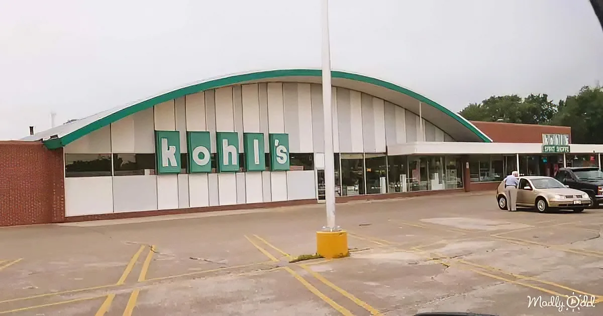 A Kohl's store with a curved roof and green sign stands in a parking lot with a few cars and a person.