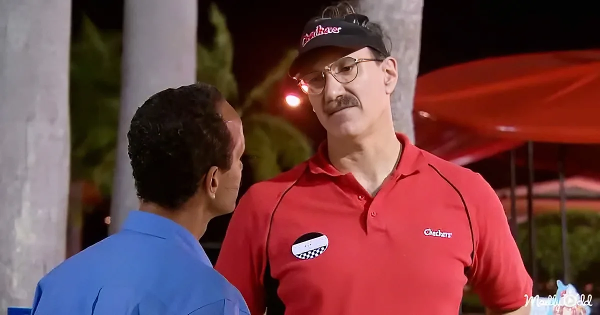 A man in a red Checkers uniform talks to another man in a blue shirt.