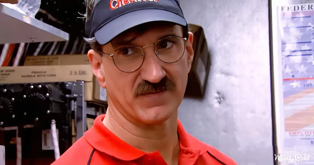 A man in a red shirt and black cap with "Checkers" logo looks to the side in a diner setting.