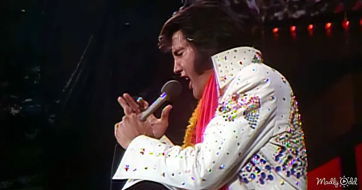 A performer in a glittery white suit sings into a microphone on stage.