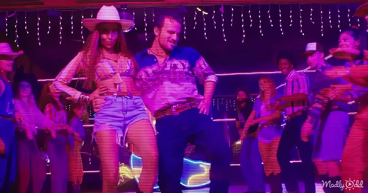 A man and woman in cowboy attire dance energetically under string lights, surrounded by a lively crowd.