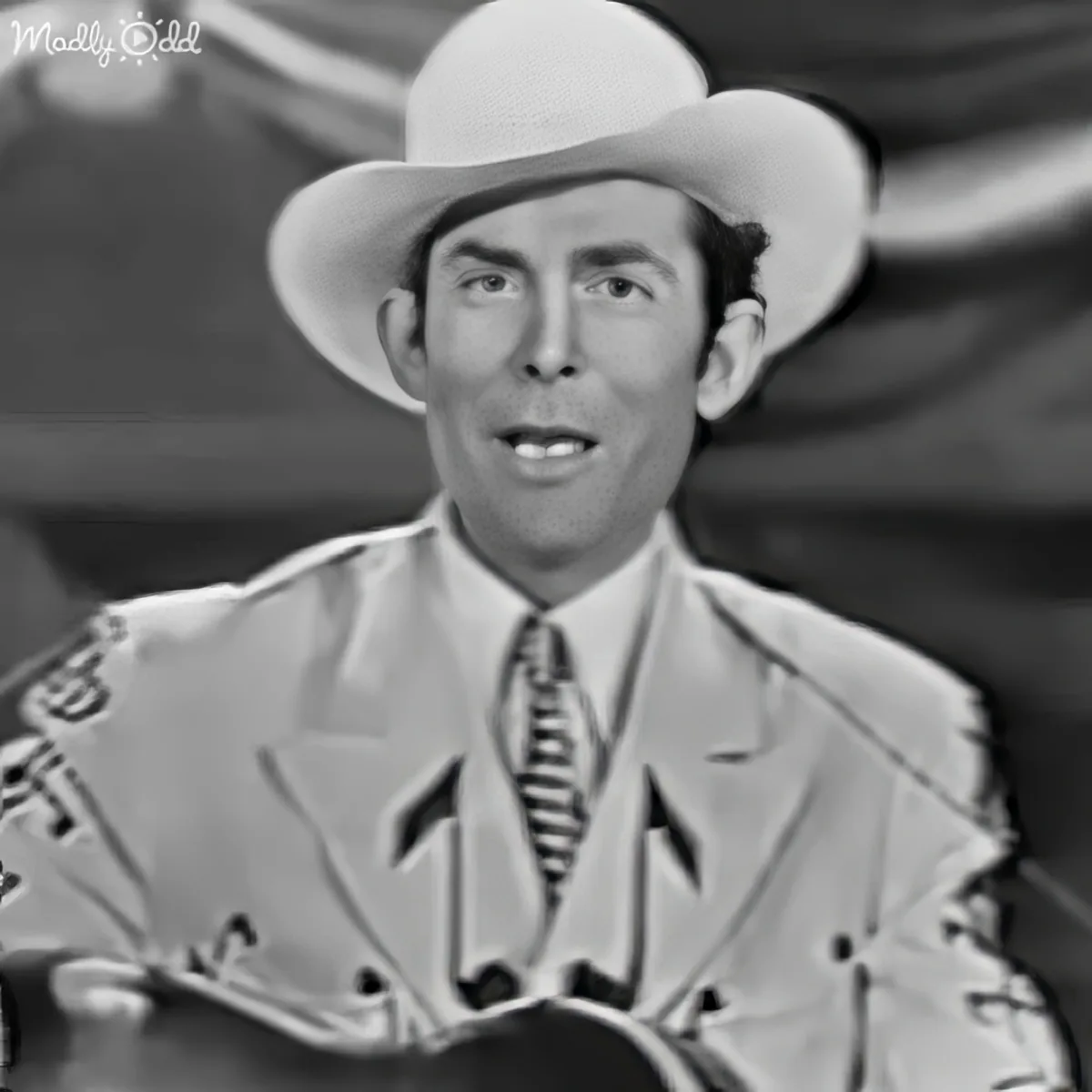 A man in a cowboy hat and patterned suit jacket is looking to the side.