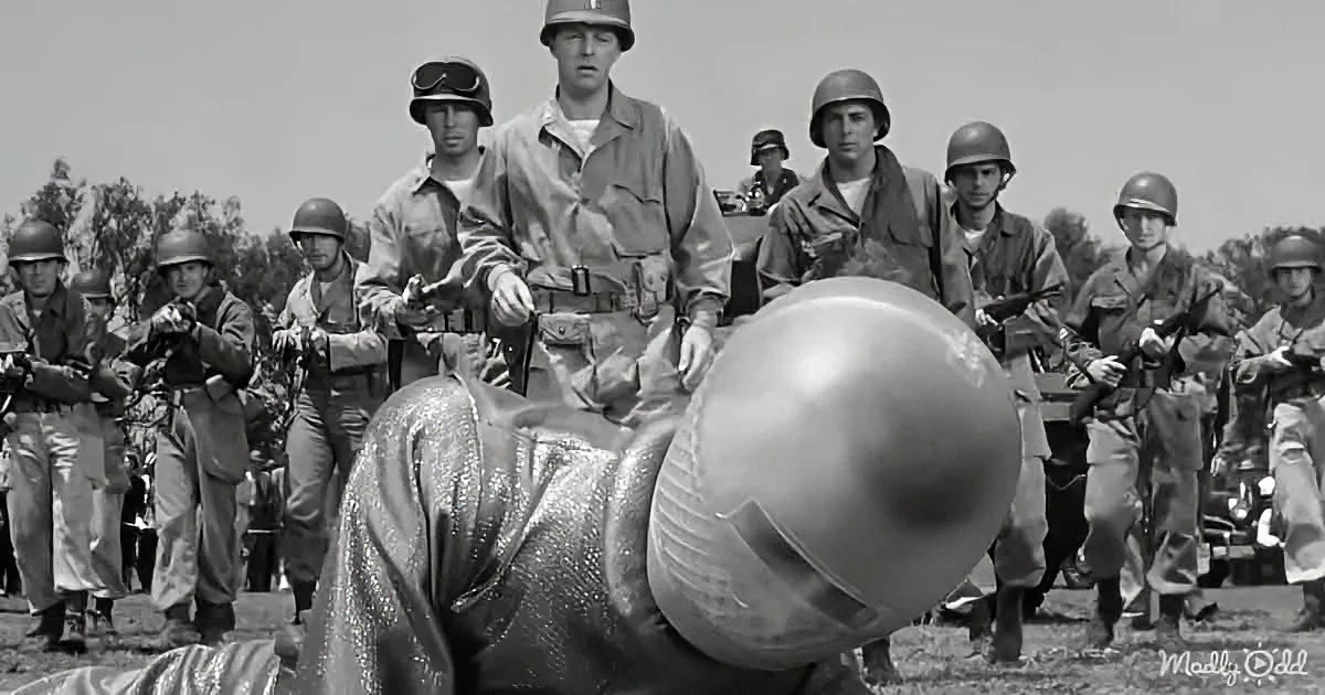 A soldier in a shiny, reflective suit is surrounded by uniformed soldiers holding weapons.