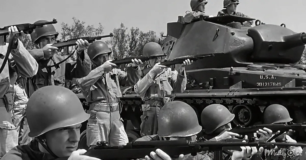 Soldiers aim rifles, one tank in the background, helmets and uniforms visible.