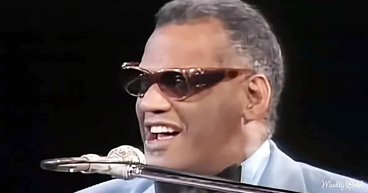 A man in sunglasses and a suit sings into a microphone, with a dark background.