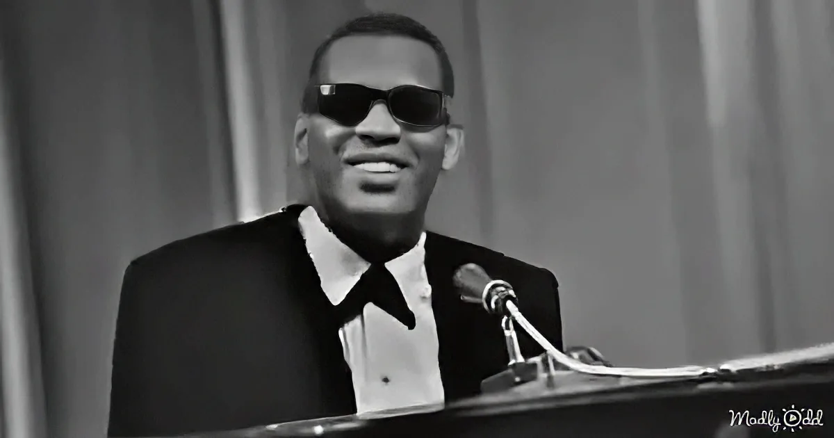 A man in sunglasses and a suit smiles at a microphone, playing a piano.