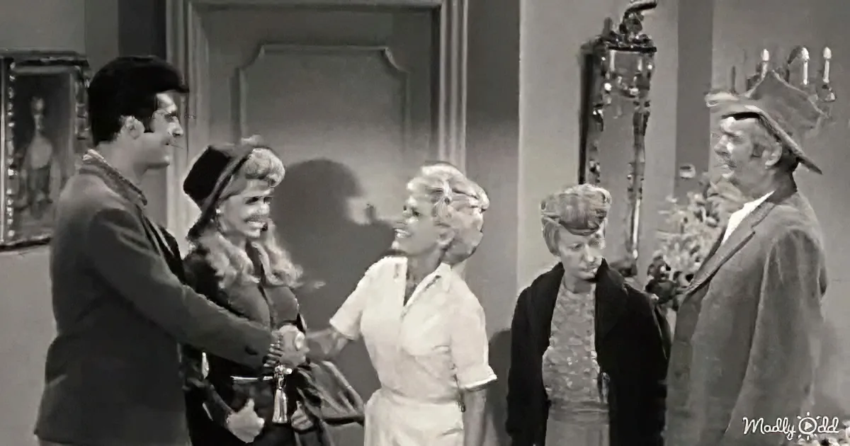 A man in a pirate costume shakes hands with a woman in a nurse outfit, surrounded by other characters in a room.