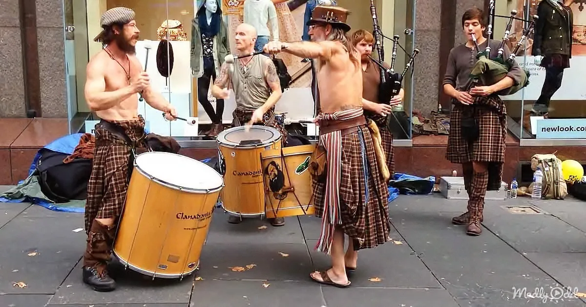 Musicians in kilts play drums and bagpipes on a city street.