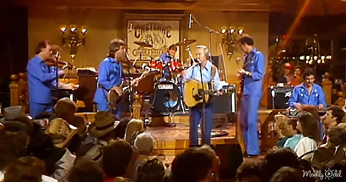 A band in blue plays on stage, surrounded by a lively audience in a cozy venue.