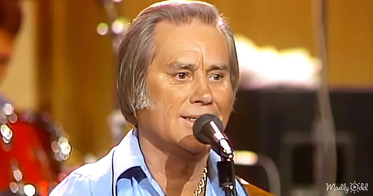 A man with gray hair and a blue shirt sings into a microphone on stage.