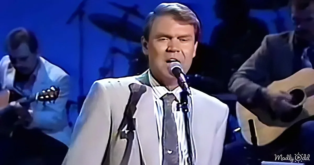 A man in a white suit sings into a microphone, with musicians in the background.