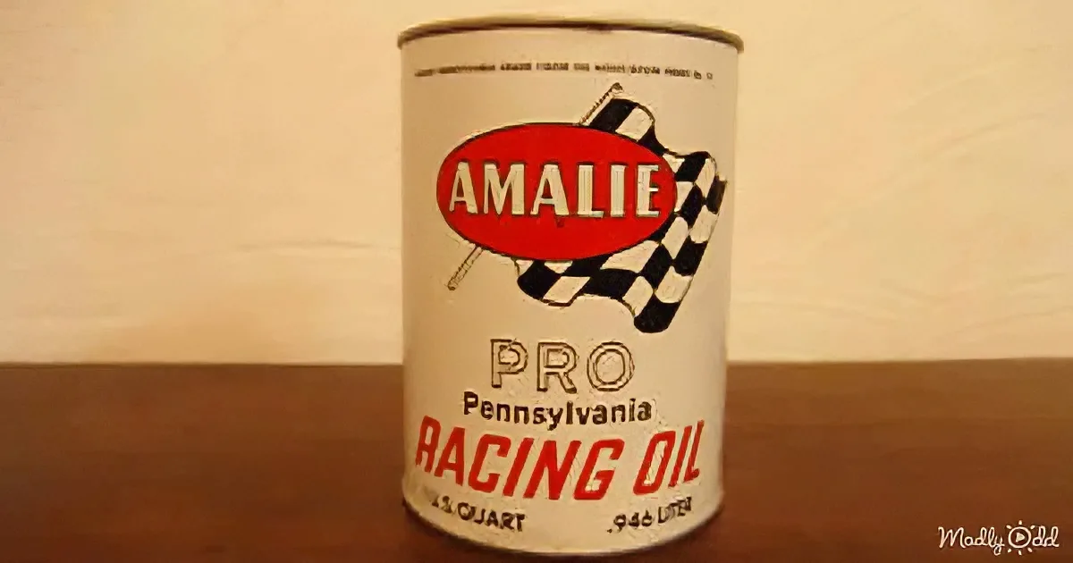 A vintage Amalie Pro Pennsylvania Racing Oil can sits on a wooden surface against a plain wall.
