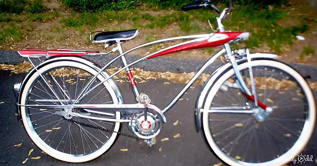 A vintage red and white bicycle with a chrome frame and white-walled tires is parked on a paved path.
