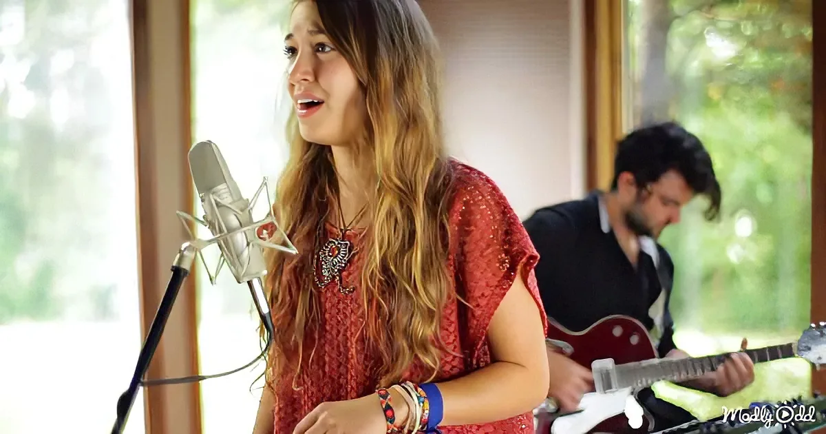 A woman in a red dress sings into a microphone, accompanied by a guitarist in the background.