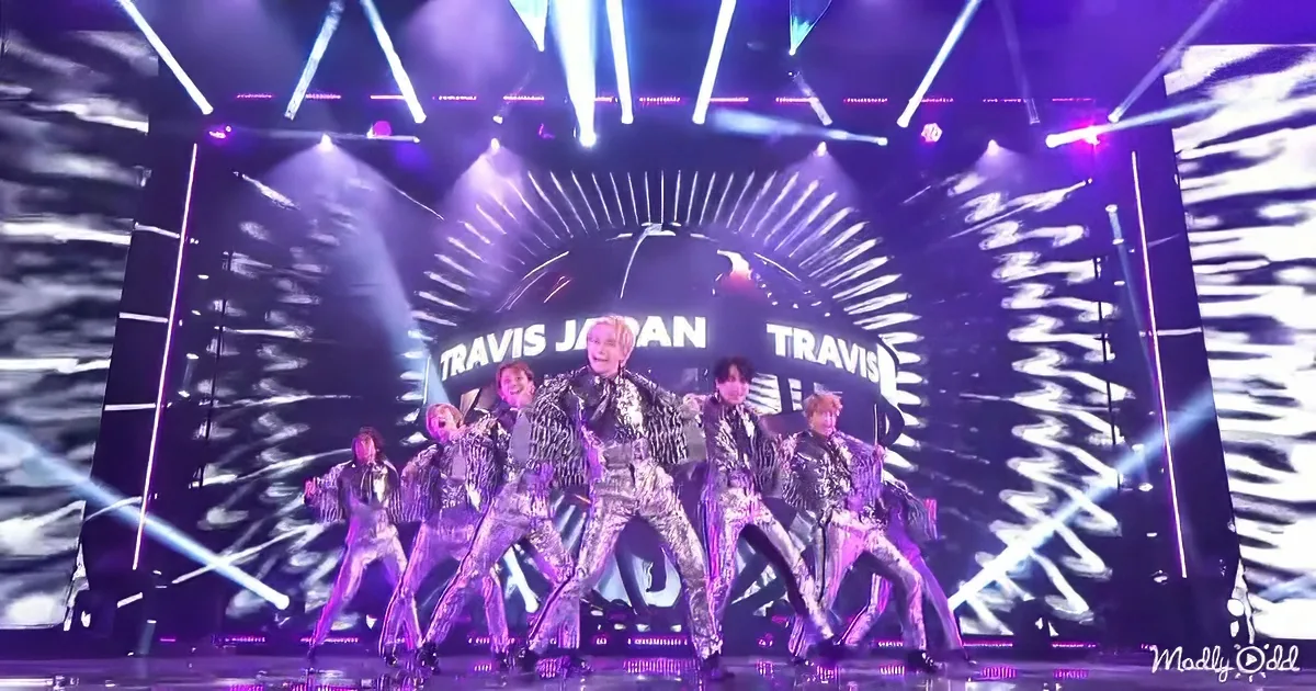 Travis Japan performs on stage in shiny outfits, surrounded by dynamic lighting and a large screen.