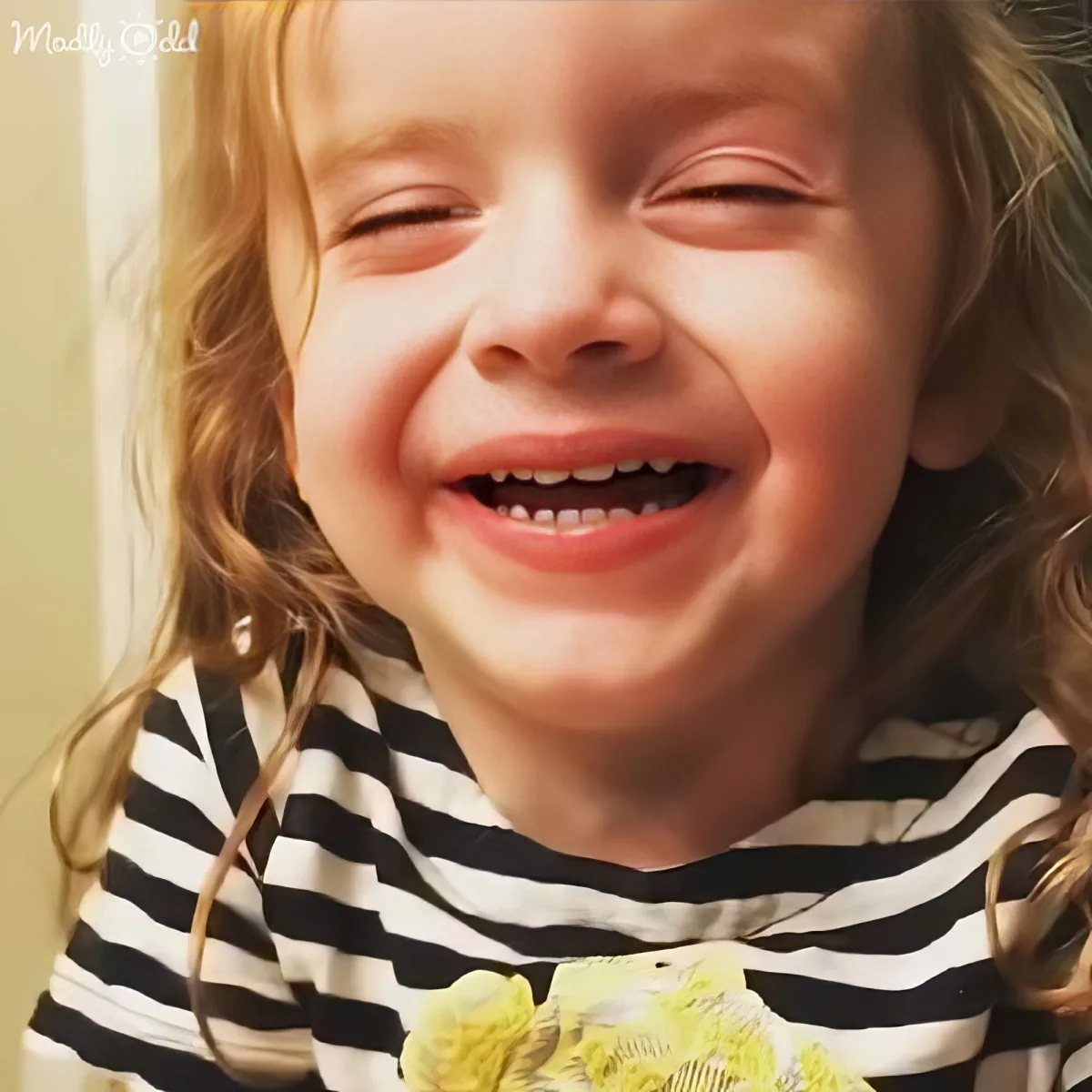 A child with curly hair and a striped shirt is laughing heartily.