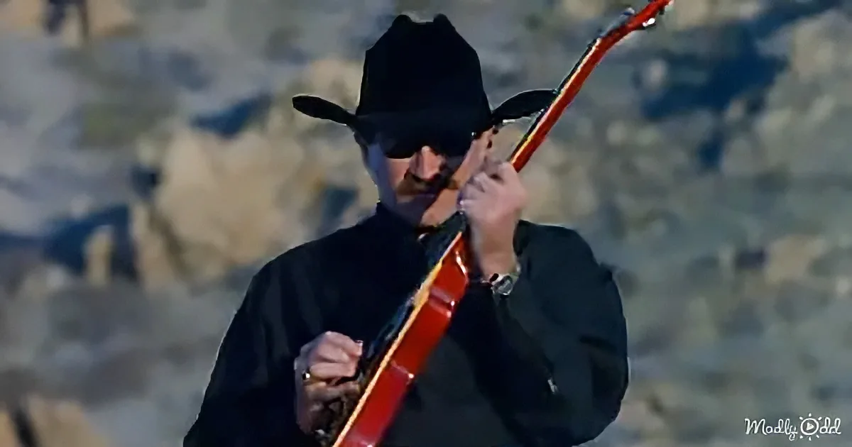 A man in a black cowboy hat and shirt plays a red electric guitar.