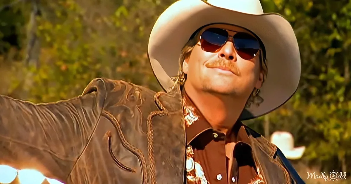 A man in a cowboy hat and leather jacket is smiling and looking up, with trees in the background.