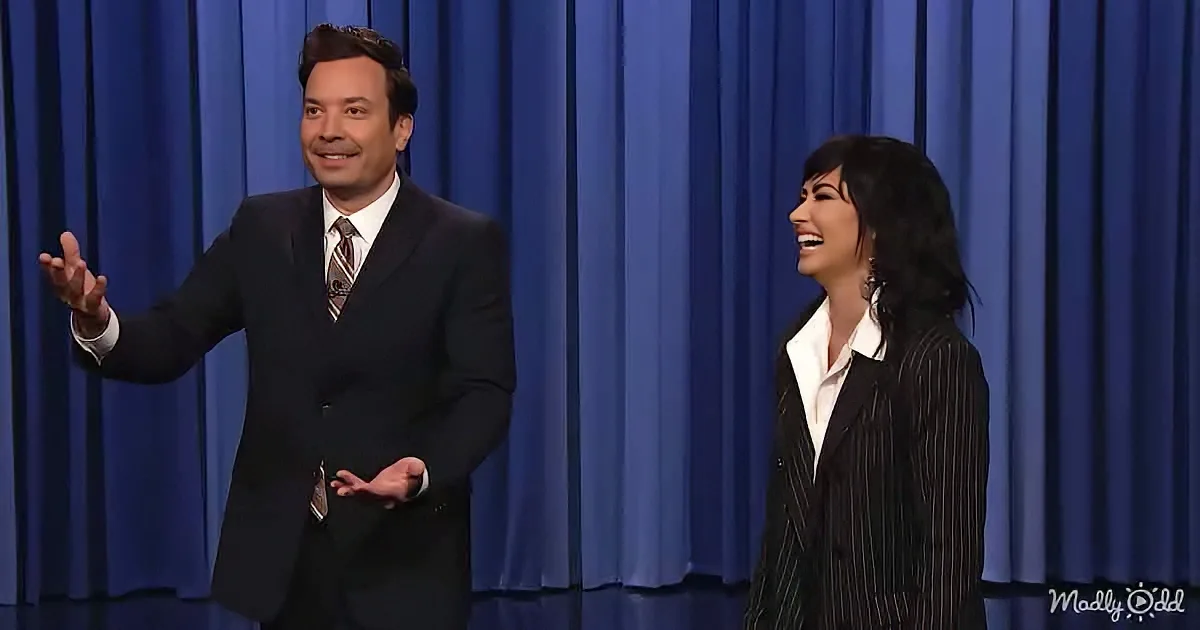 A man in a suit gestures while a woman in a striped suit laughs on stage.