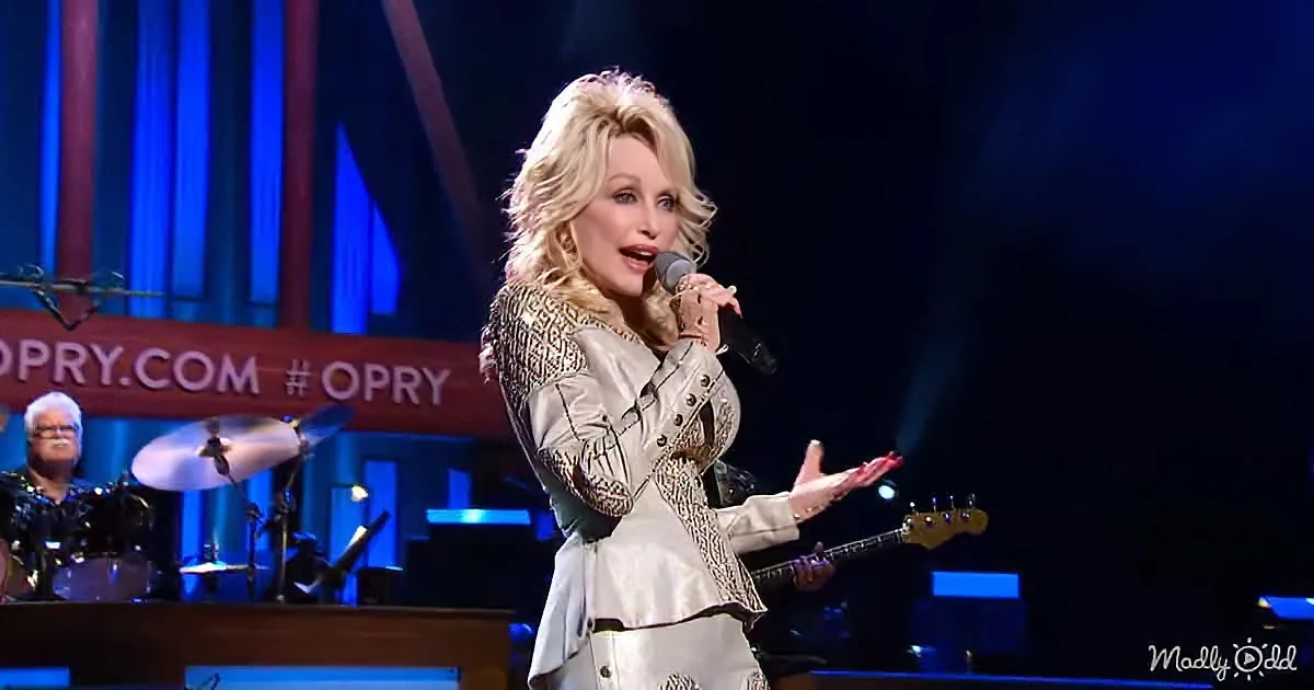 Dolly Parton sings on stage in a white outfit, holding a microphone, with a band behind her.