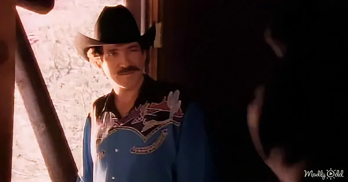 A man in a cowboy hat and blue shirt stands in a doorway, looking to the side.