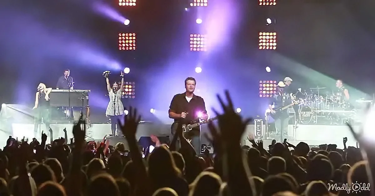 A band performs on stage with vibrant lights, surrounded by an enthusiastic crowd raising their hands.