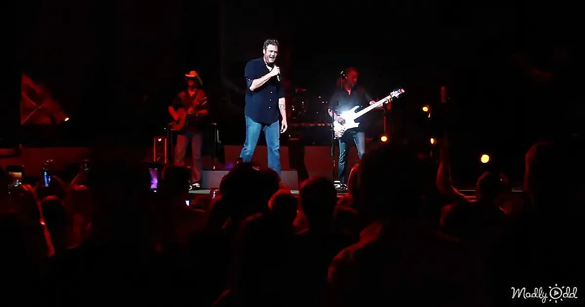 A man sings on stage with musicians, audience in dim light.