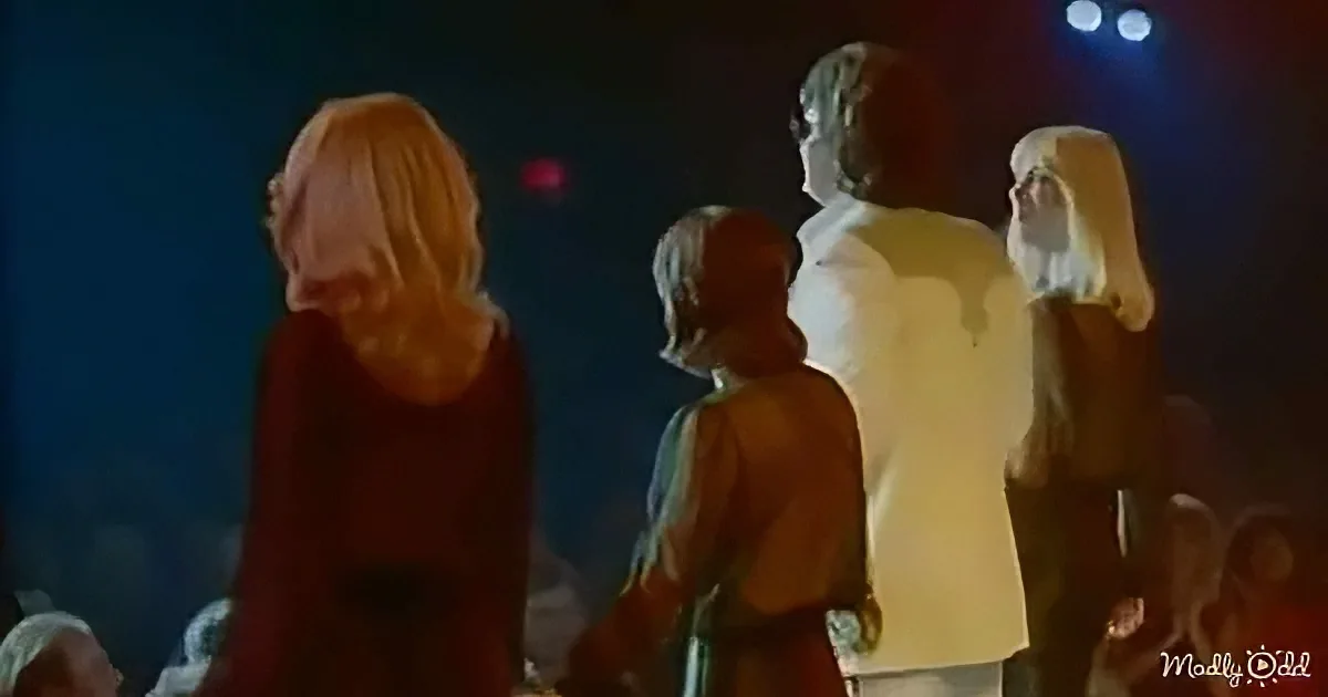 A group of people, including a child, stands in a dimly lit room, facing away from the camera.